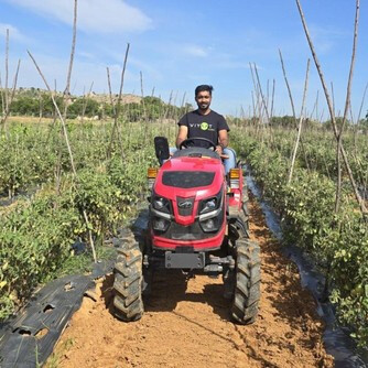 Yakshith Kiran driving a tractor between crop rows on a farm